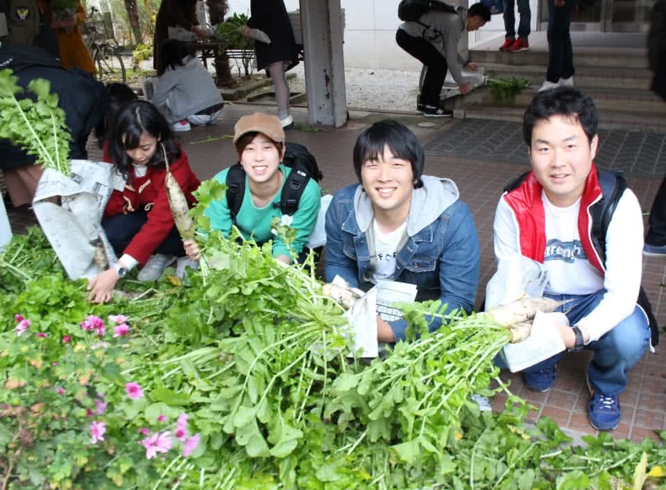 写真：無料野菜スタンドで並べられた野菜とそれを手に持つ学生たち