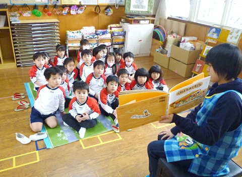 写真：絵本の読み聞かせをする先生と、熱心にそれを聞く園児たち