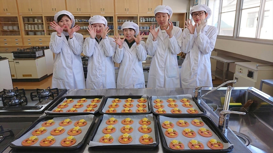 写真：バットに並べられたみまっぱクッキー。その後ろに並ぶ5名の学生