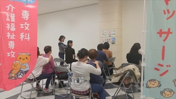 写真：椅子に座って地域の人の方をマッサージする学生