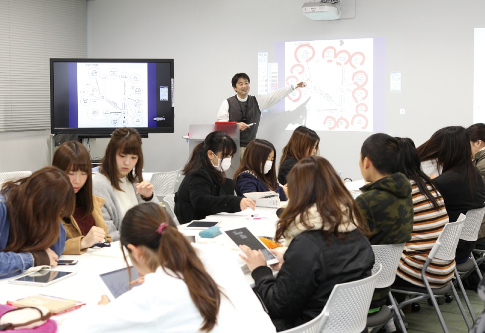 写真:社会福祉について授業を行う教員と、タブレット等を使用しながら講義を受けている学生たち
