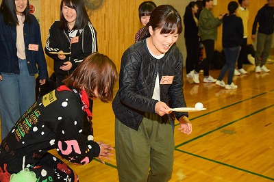 体育館でピンポン玉を運ぶゲームをする学生