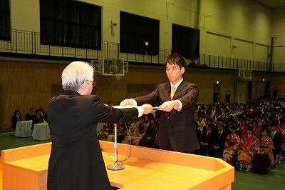 写真：学長から卒業証書を授与され、受け取る学生