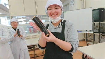 写真：手巻き寿司を持って、こちらに見せる1名の学生