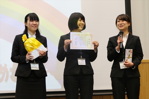 写真：表彰式で、表彰状と記念品をみんなに見せる3名の学生