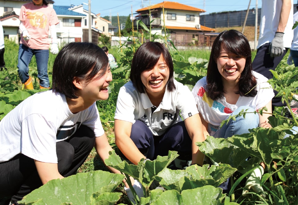 写真:自然体験活動で畑にしゃがんでいる3人の女子学生