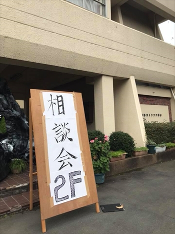 写真：会場の建物の前に「相談会」と書かれた看板が置いてある様子