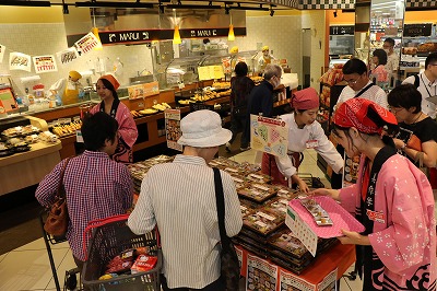 写真：マルイ店内で弁当を販売する学生と、売り場を見る買い物客