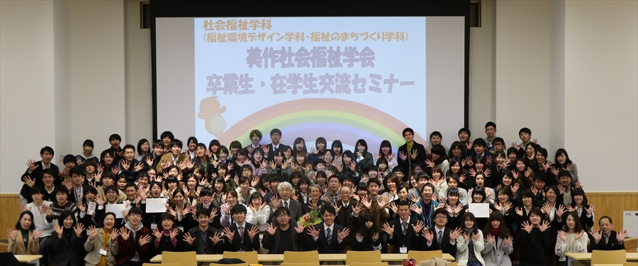 写真：卒業生・在校生交流セミナーと書かれたスライドの前で両手を広げる参加者