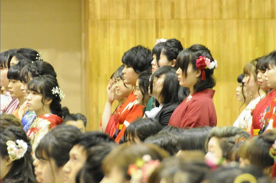 写真：卒業式中に、起立して代表者が卒業証書を受けるの見守る学生