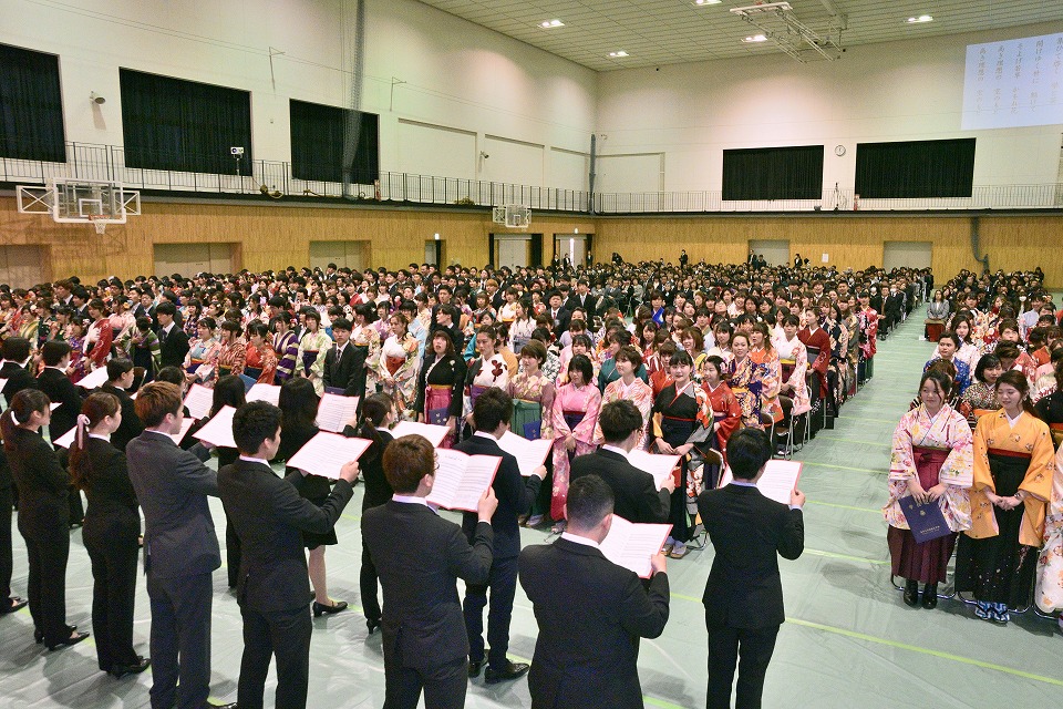 写真：後輩たちの合唱隊の学歌斉唱を聞く卒業生たち