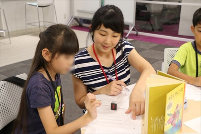 写真：女子学生が小学生に寄り添って書き方を指導する様子