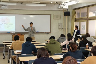 写真：教室の教壇で話す野々上真伸氏と、聴講する学生