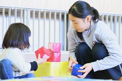 写真：手作りのブロックを使って遊ぶ学生と子ども