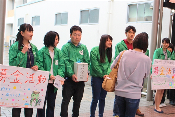 写真：募金箱を持って募金を呼びかける学生と、その前を通る学生