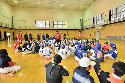 写真：体育館内では小学校低学年の受講者にボールを投げるポイントを説明するひろせ選手と伊藤選手