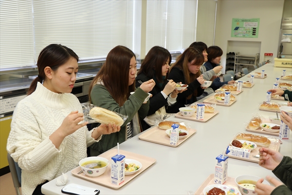 写真：机を挟んで、学生たちが給食を食べる様子