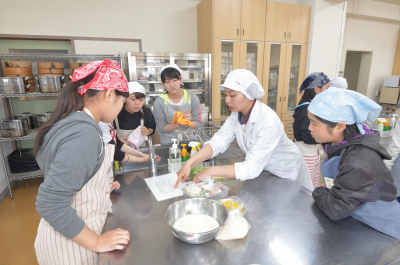写真：班ごとに分かれて調理実習、先輩の説明を聞く新入生5人