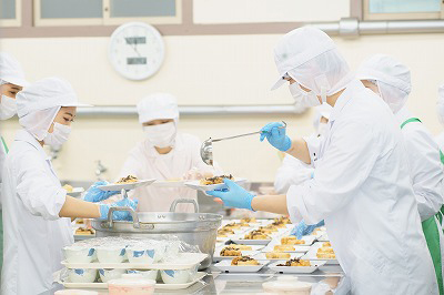 写真：大量調理中、盛り付け作業を担当する学生