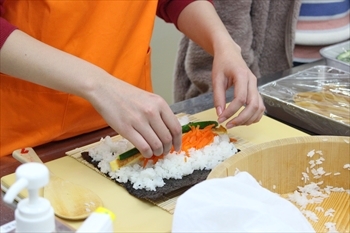 写真：ご飯の上ににんじんときゅうりと卵を置いて、手巻き寿司を巻く様子