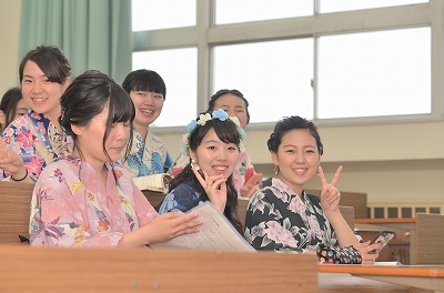 写真：a授業前に席に座り、こちらに向かってポーズする6名の浴衣姿の女子学生