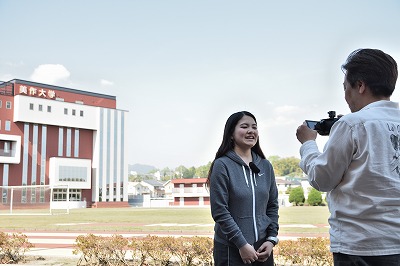 写真：100周年記念館をバックにメッセージビデオを撮影する学生とディレクター