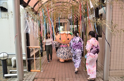 写真：aマスコットキャラクターのミマッパちゃんの着ぐるみが登場。七夕飾りの下を通って食堂に向かう姿