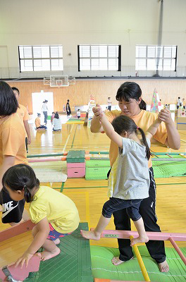 写真：遊具で遊ぶ子どもの手を引き、安全に注意しながら遊ぶ女子学生