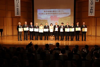 写真：ステージ上に協定書を持って並ぶ岡山県民局と10市町村、津山高専、美作大学の代表者