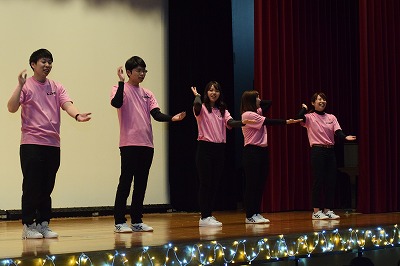 ステージ上で子供の手遊びの歌を歌う学生