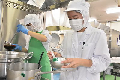 写真：管理栄養士役の学生が味噌汁の塩分濃度を計測している