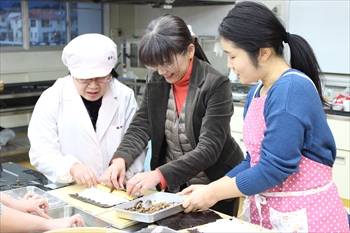 写真：手巻き寿司を巻く藤井教授と職員と学生