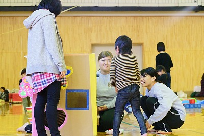 写真：段ボールでできた遊具で遊ぶ学生と子どもと親