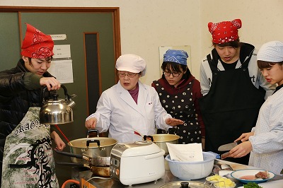 写真：コンロに掛けられた鍋の前で説明する藤井教授と、それを聞く学生たち