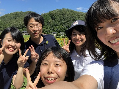 写真：ひまわり畑で学生と記念撮影をする作野先生