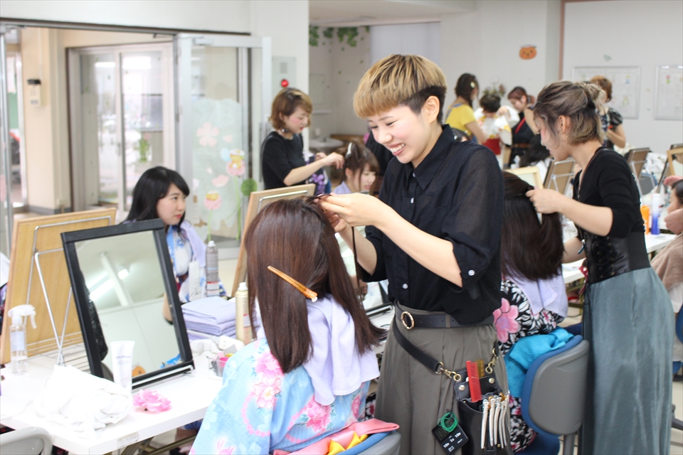 写真：ヘアセットをする美容師と、髪を結ってもらう学生