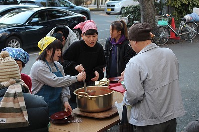 写真：炊き出しボランティアの様子。炊き出しを取りに来た人とコミュニケーションをする学生たち