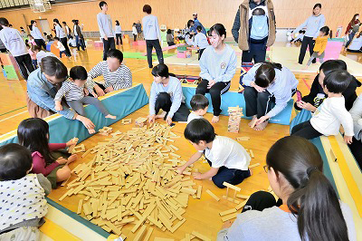 写真：手作りの積み木を使って遊ぶ親子連れと学生