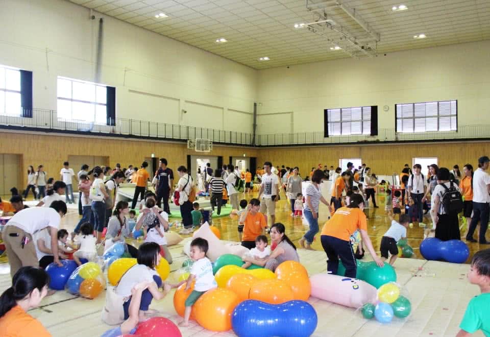 写真:体育館に設置された様々な手作りの遊具で遊ぶ大勢の親子と対応する学生たち