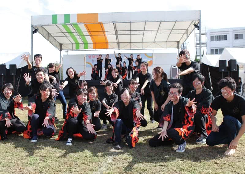 写真:野外ステージの前で両手を広げたポーズで写真に収まる岡山県人会のメンバーたち