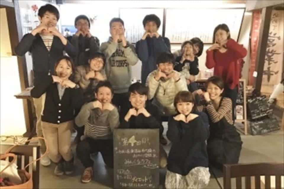 写真:みんくるカフェの会場で「M」のポーズを手で作る、学生と教員と参加者
