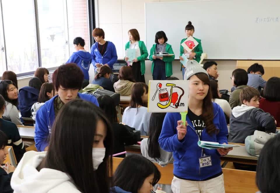 写真:教室で着席している新入生と、立っているオリゼミスタッフの学生たち。イラストが描かれた札を持っているオリゼミスタッフの学生もいる。