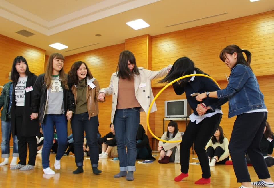 写真:横一列に並びフラフープを順にくぐり抜けるゲームを行っている学生たち。