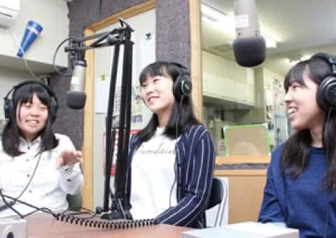 写真：スタジオでヘッドフォンを付けラジオ放送する3人の女子放送研究サークルのメンバー