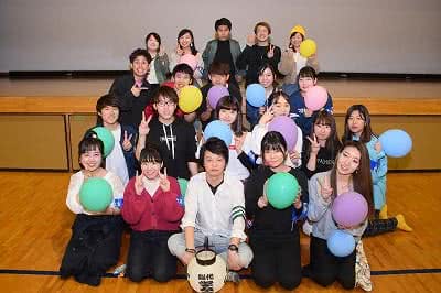 写真:体育館の壇上の前に集合し、両手を広げたポーズで集合写真に収まる学友会のメンバーたち