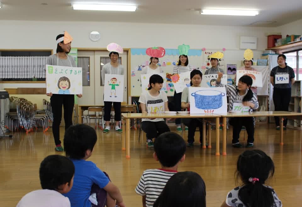 写真:食べ物のお面をつけた学生達が紙芝居等で幼稚園児に食についてお話をしている様子