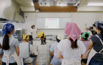 写真:料理教室の様子。ホワイトボードで説明する森本先生とそれを聞く子どもたち。