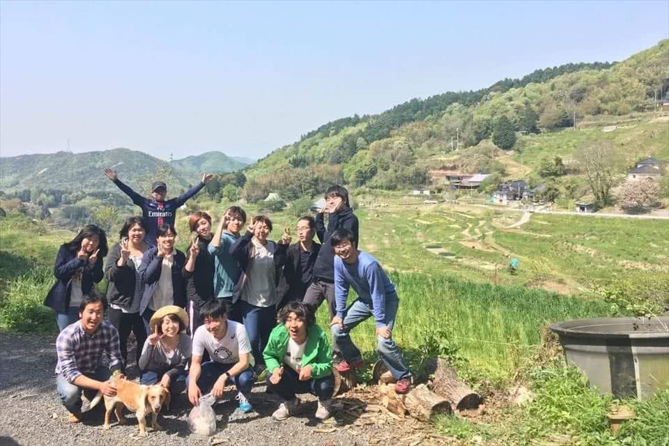写真:棚田と青空を背景に、学生と教員と地域の方がピースをしている様子