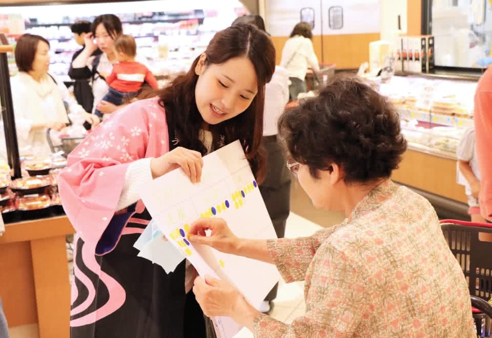 写真:マルイノースランド店にて実施した共同開発弁当販売キャンペーンでお客さんにアンケートに答えてもらう人見研究室の学生