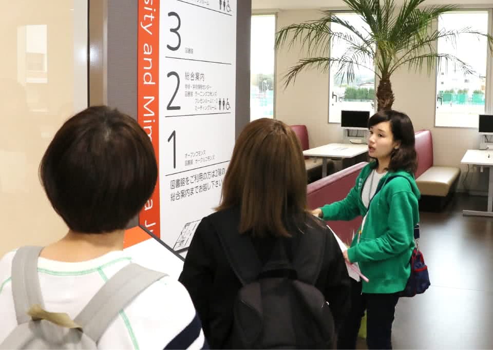 写真:階の案内板のそばに立つ3人の女子学生